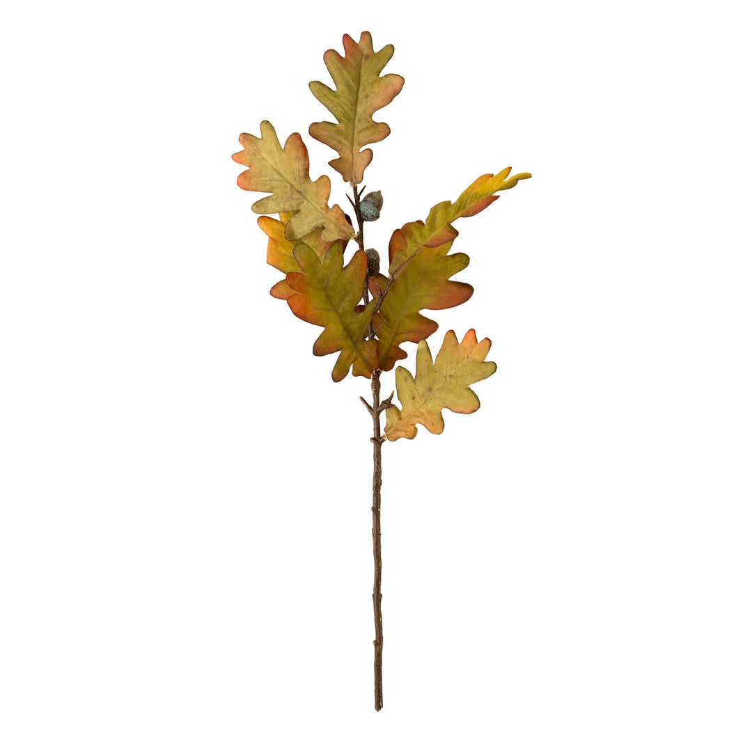 An artificial oak leaf branch with realistic leaves in shades of green, yellow, orange, and brown, attached to a brown stem, shown against a solid cream background.